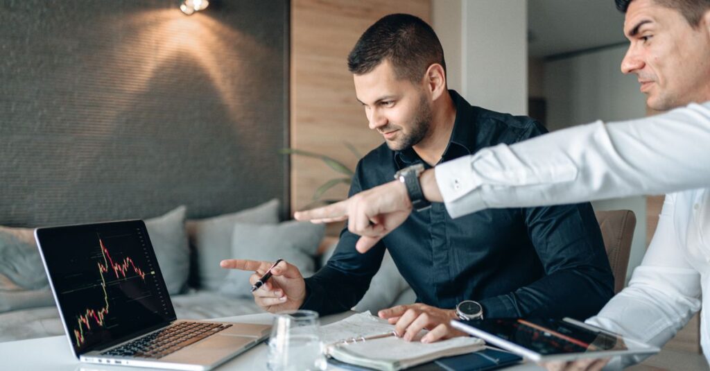 Dois homens discutindo dados financeiros em um laptop em um ambiente de trabalho moderno